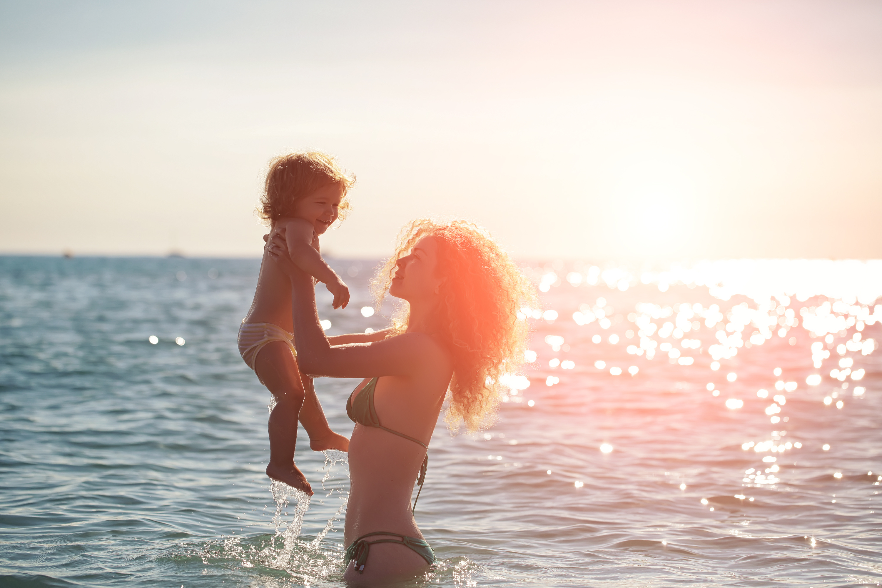 Maman et son bébé dans l'eau de mer face à un couché de soleil